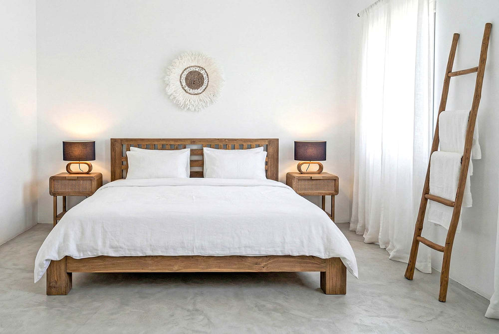 Wooden bed with white bedding in a minimalistic bedroom setting.