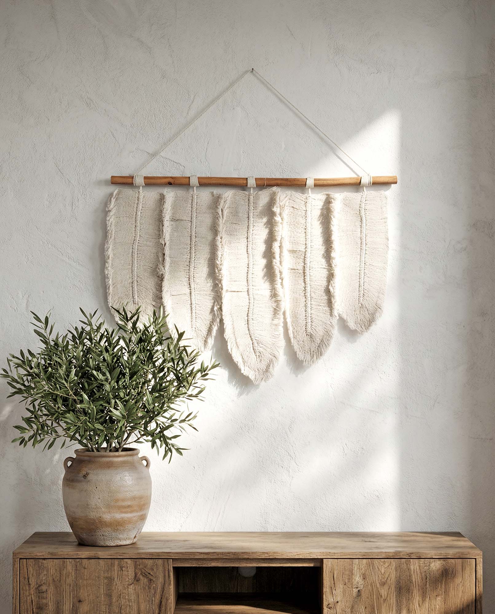 Woven wall hanging on a white wall with a potted plant and wooden cabinet below.