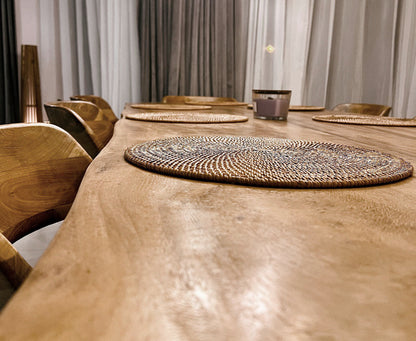 A natural color round rattan table mat with intricate weaving techniques on a wood table.