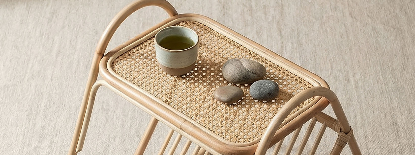 Wicker side table with a small green cup and stones on a beige background