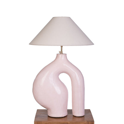 A ceramic base table lamp with an asymmetrical shape and a linen lampshade, in a white background. 