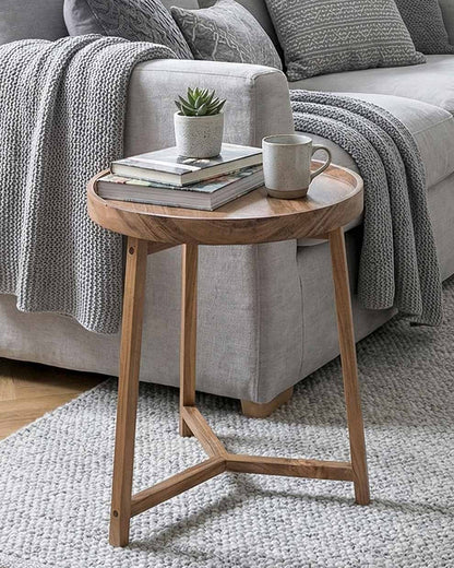 Wooden side table with a cup, books, and plant in front of a gray sofa.
