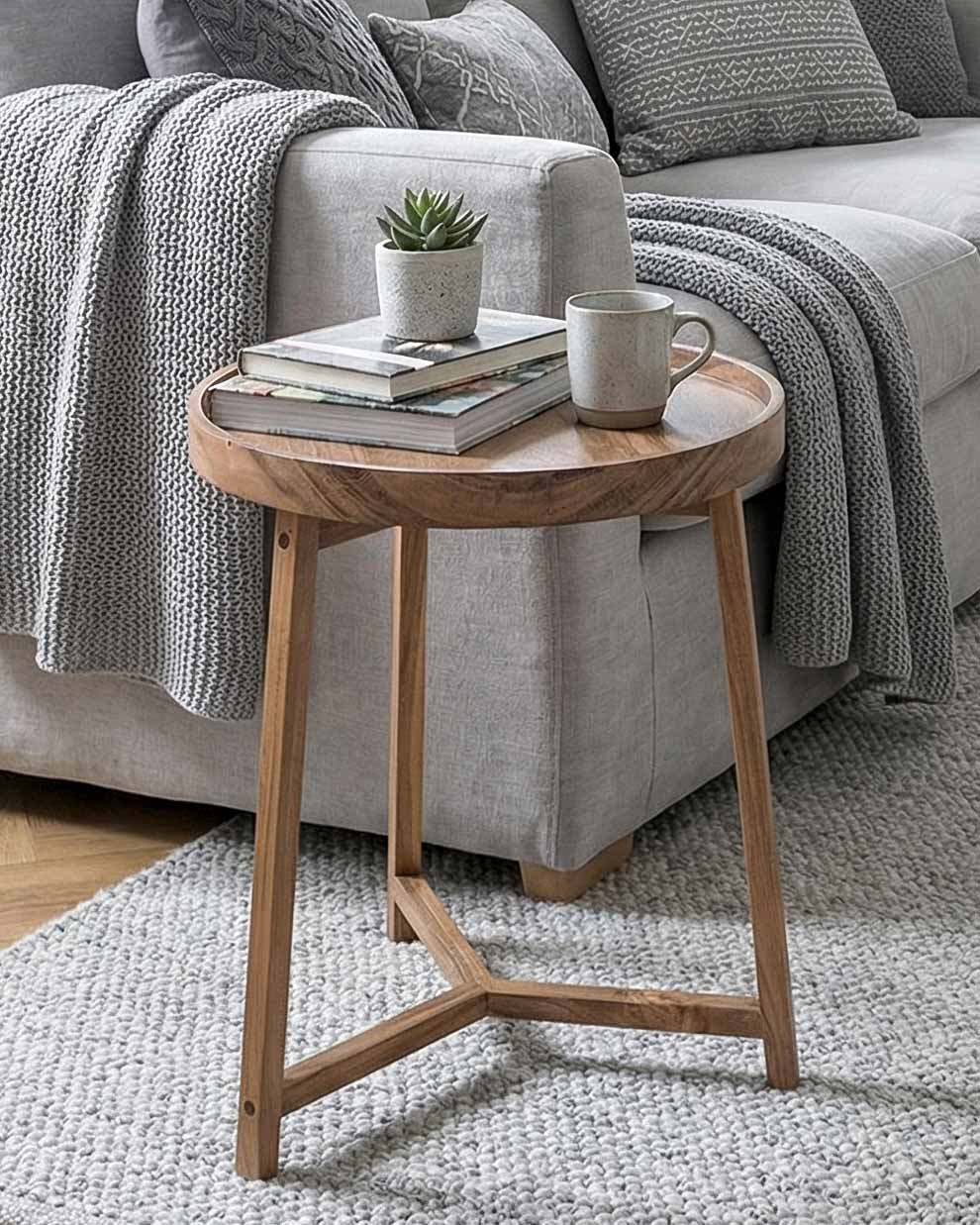 Wooden side table with a cup, books, and plant in front of a gray sofa.