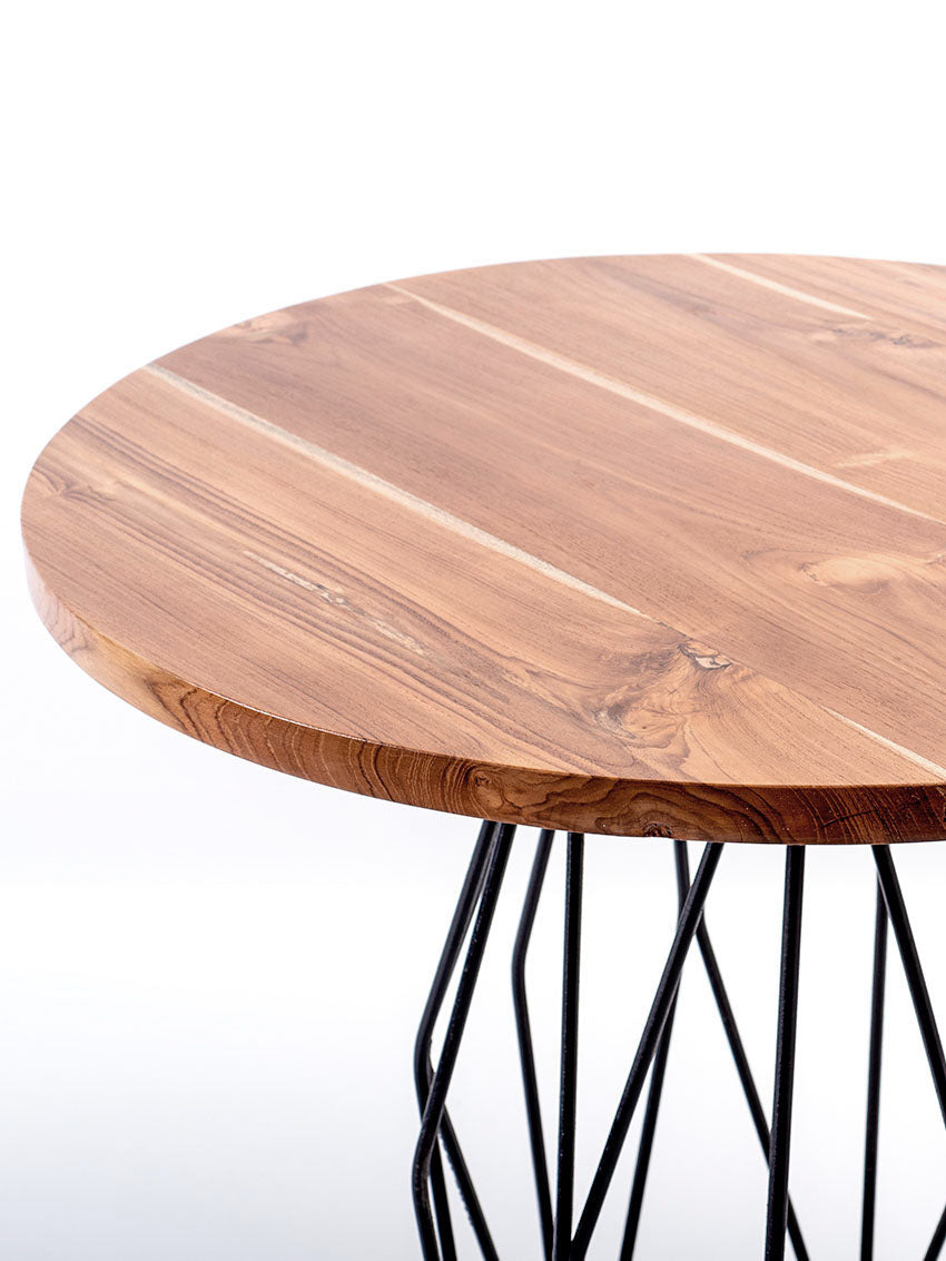 Round bar table with a natural wood finish on the tabletop and a black geometric metal base. Top view.