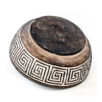 A hand-carved wooden bowl with geometric patterns, primarily in brown color with white accents.