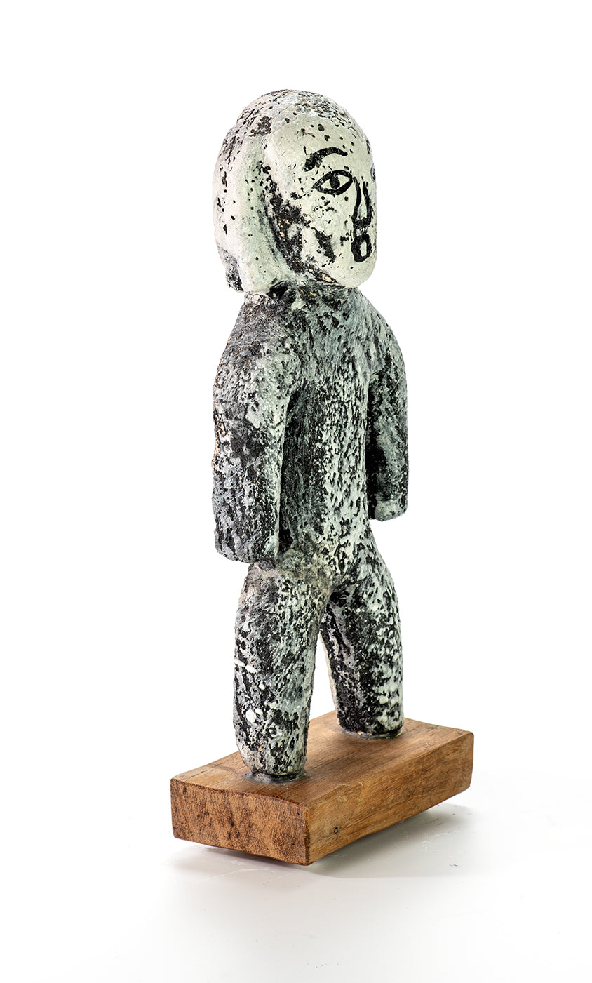 Handmade ceramic miniature figure of a person with a finish resembling ancient stone artifacts, displayed on a wooden stand.