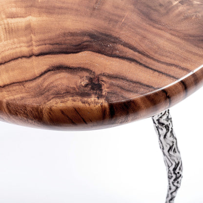 A round teak wood coffee table with a glossy finish and metal support legs with a relief structure. Closeup detail view. 