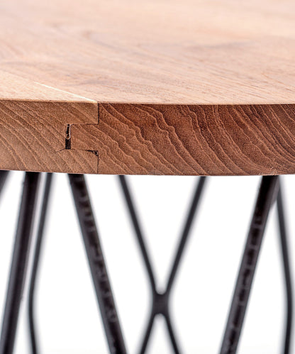 A round suar wood coffee table with a matte finish on a black metal base.