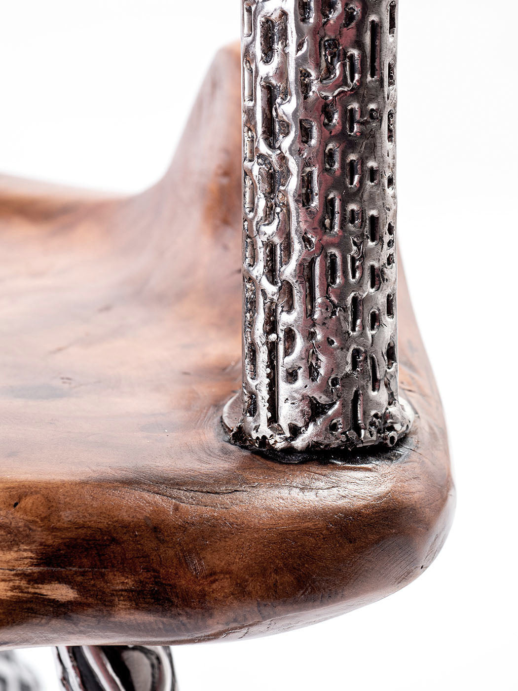 An artistically designed dining chair with a glossy finish on a white background. The chair features a teak wood seat and stainless steel legs with a relief longitudinal structure. Closeup detail. 