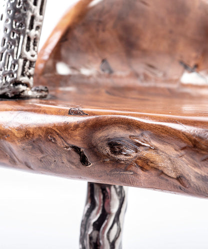 An artistically designed dining chair with a glossy finish on a white background. The chair features a teak wood seat and stainless steel legs with a relief longitudinal structure. Closeup detail view. 