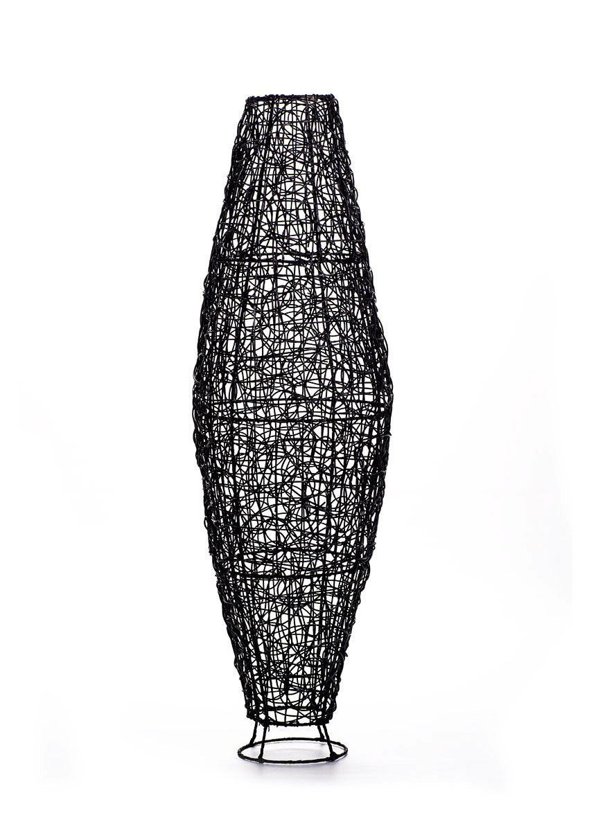 A tall black rattan floor lamp with a tapered design, complete with a base and a cable, against a white background.