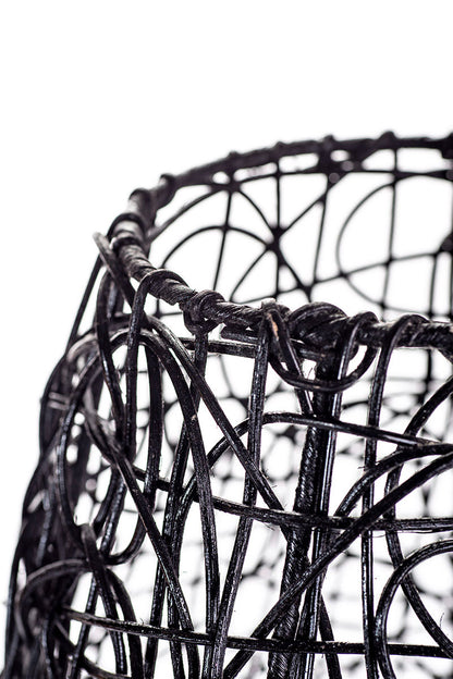 A tall black rattan floor lamp with a tapered design, complete with a base and a cable, against a white background.