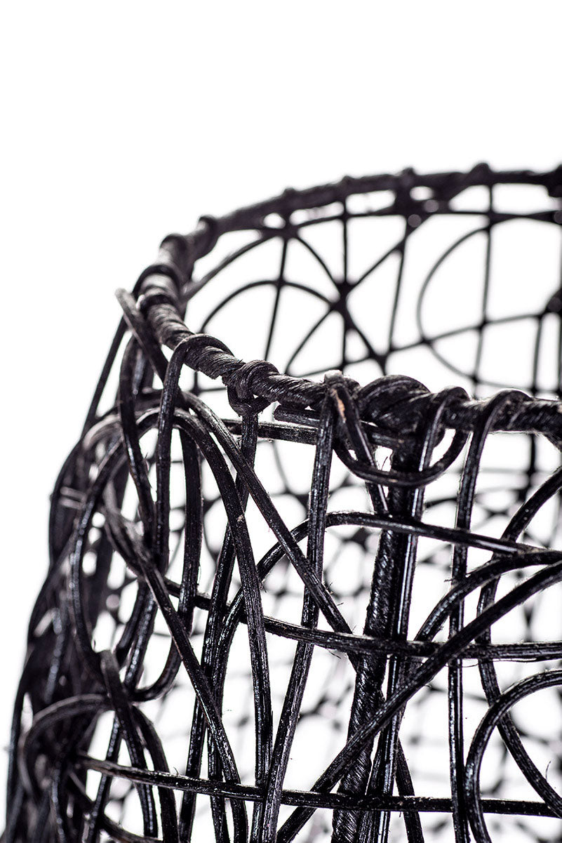 A tall black rattan floor lamp with a tapered design, complete with a base and a cable, against a white background.