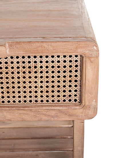 Close up look of small one-drawer teak wood side table with rattan netting on the front and a lower shelf, set against a white background.