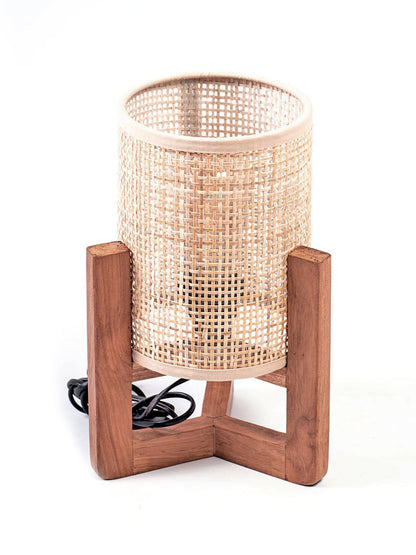 A table lamp with a teak wood base and a cylindrical antique rattan shade, with a visible power cable.