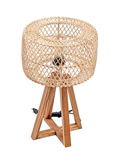 A table lamp with a rattan weave lampshade and a teak wood base, standing on a tripod base with a cable attached.