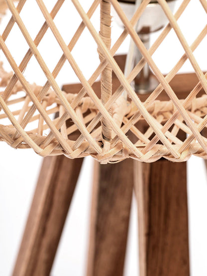 A table lamp with a rattan weave lampshade and a teak wood base, standing on a tripod base with a cable attached.
